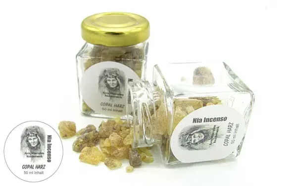 Zwei kleine Glasfläschchen mit Copal-Harz der Marke Aura Mineralien, umgeben von losen bernsteinfarbenen Harzstücken.